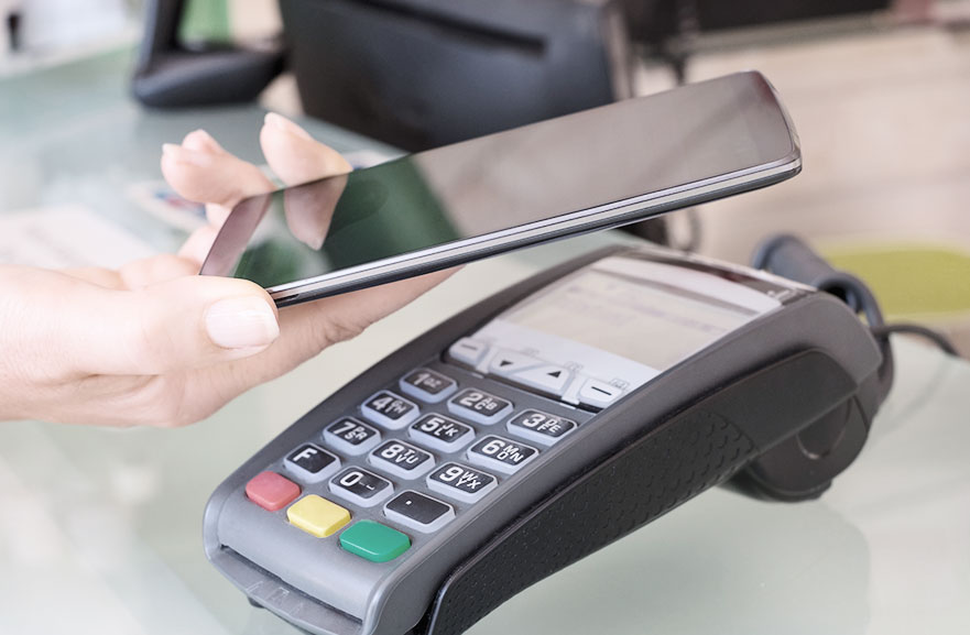 Foto de maquinainha para cartões e celular aproximando para realizar o pagamento. 