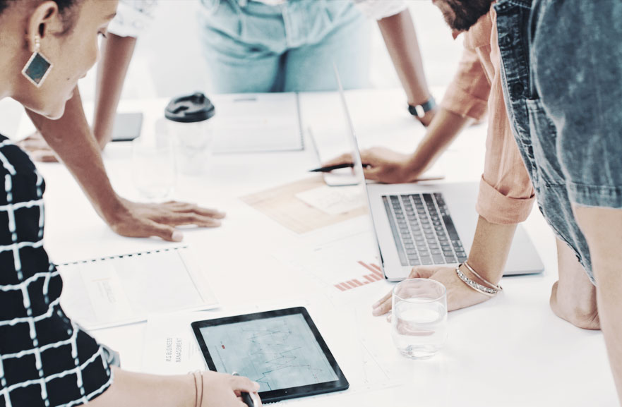 Foto de mesa com pessoas ao redor com computadores corporativos e graficos. 