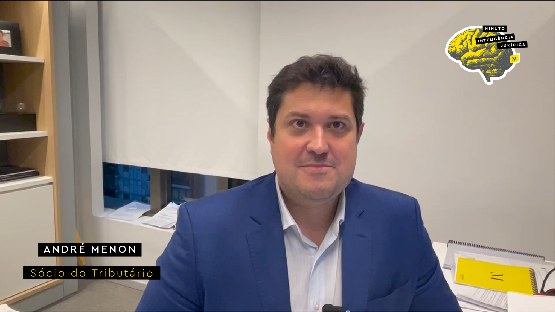 Homem olhando para a foto e sorrindo, usando terno azul marinho e camisa branca. No canto inferior esquerdo, frase com os dizeres "André Menon - sócio do Tributário". No canto superior direito, logotipo do Inteligência Jurídica