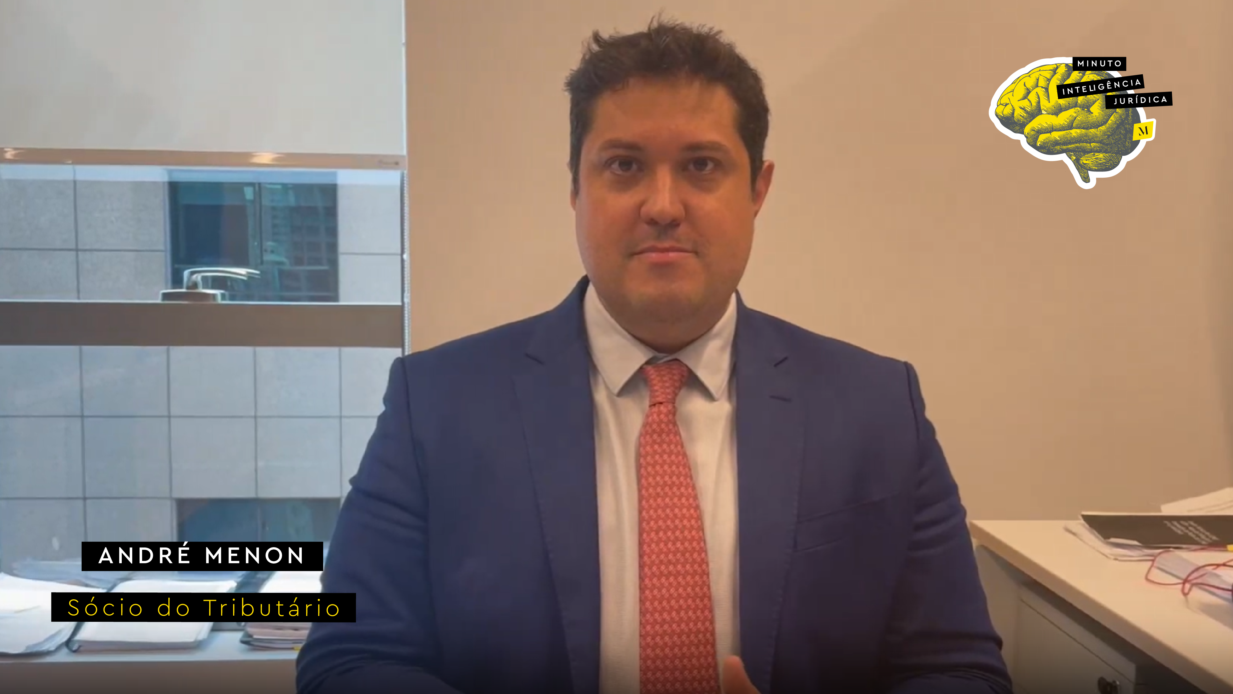 Homem com cabelo preto, usando camisa branca, gravata salmão com bolinhas brancas e blazer azul marinho. No canto inferior esquerdo, faixa preta com frase nas cores branco e amarelo escrito: André Menon, sócio do Tributário. No canto superior direito, imagem ilustrativa de cérebro amarelo com faixa de texto escrito: Minuto Inteligência Jurídica