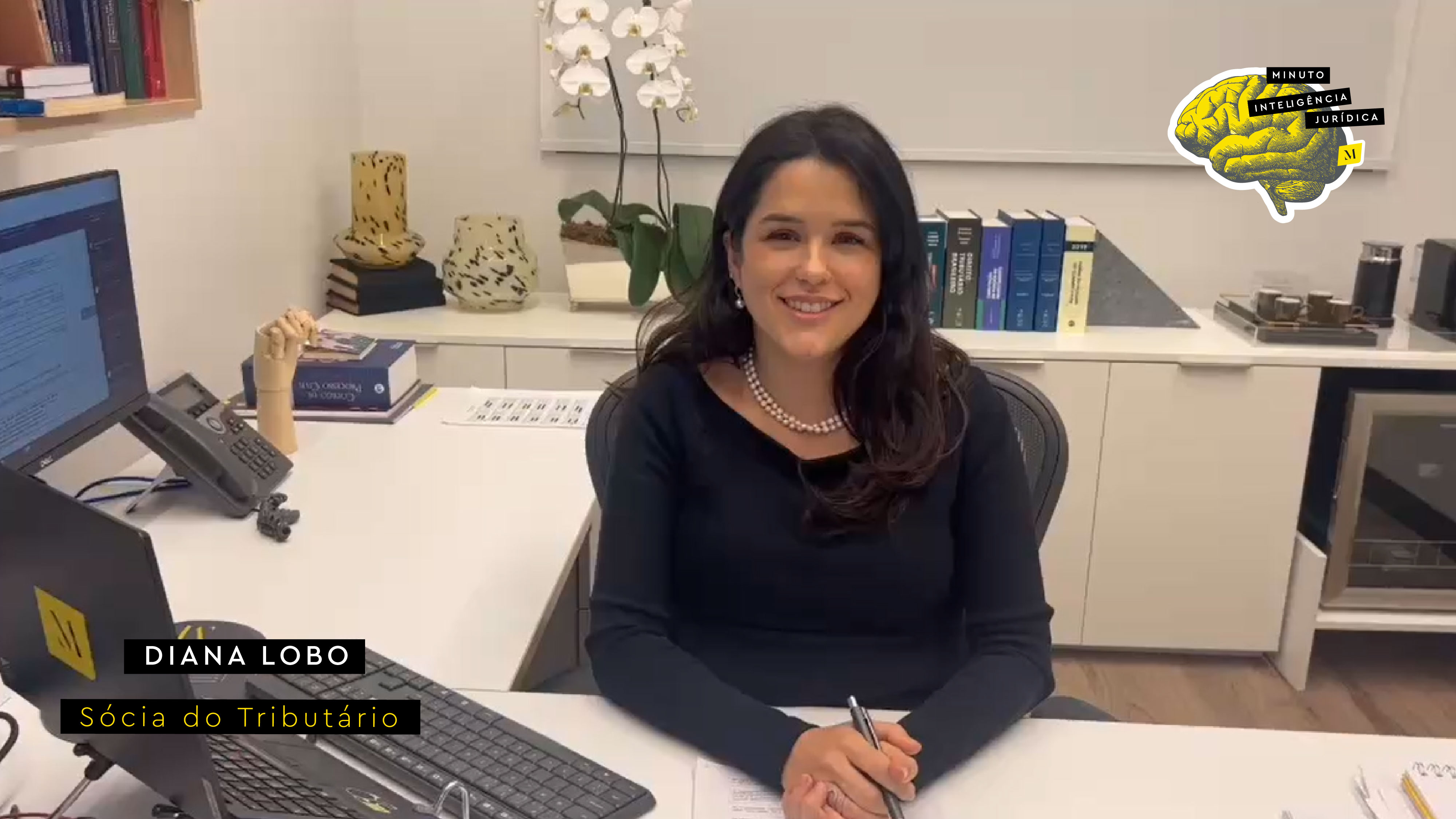 Mulher olhando para a foto e sorrindo, com cabelo preto e longo, usando vestido preto e colar de pérolas. No canto inferior esquerdo, frase com os dizeres "Diana Lobo - sócia do Tributário". No canto superior direito, logotipo do Inteligência Jurídica