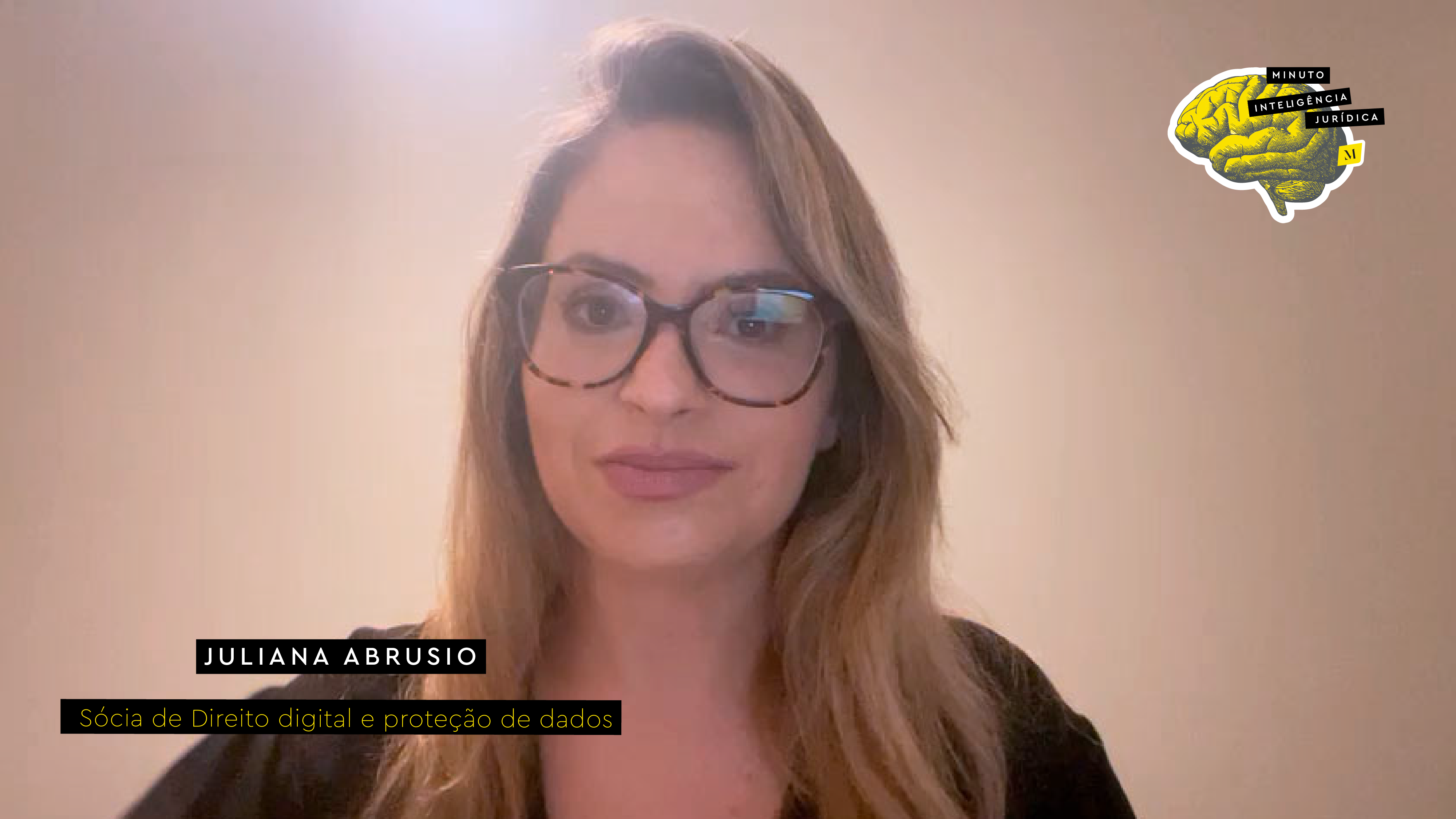 Mulher com cabelo loiro longo, usando oculos e camisa preta. No canto inferior esquerdo, faixa preta com frase nas cores branco e amarelo escrito: Juliana Abrusio, sócia de Direito digital e proteção de dados. No canto superior direito, imagem ilustrativa de cérebro amarelo com faixa de texto escrito: Minuto Inteligência Jurídica