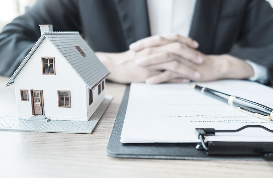 Projeção 3d de casa no formato de maquete, nas cores branco, marrom e cinza. Ao lado, prancheta com folha sulfite branca e caneta preta e dourada.