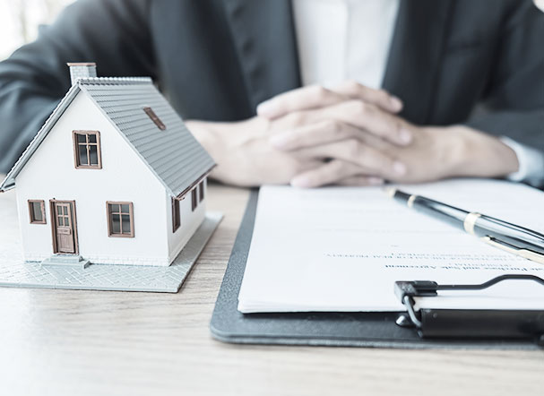 3d projection of a house in model format, in white, brown and gray. Next to it, a clipboard with a sheet of white sulphite and a black and gold pen.