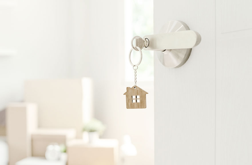 chave residencial com um desenho de uma casa de madeira como chaveiro. A chave está presa à maçaneta da porta