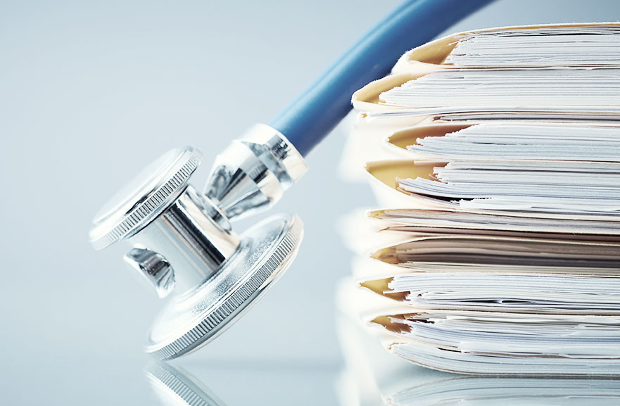 Estetoscópio com cordão azul marinho e ponta prateda posicionado acima de uma pilha de papéis