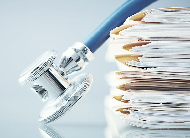 Stethoscope with navy blue cord and silver tip positioned above a stack of papers