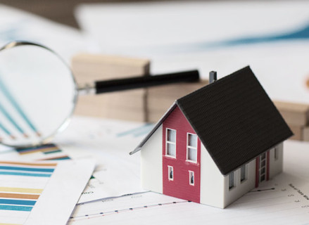 Illustration of a white house with a red stripe between the windows and a black roof. Next to it, magnifying glass and A4 sheets of paper with printed graphics
