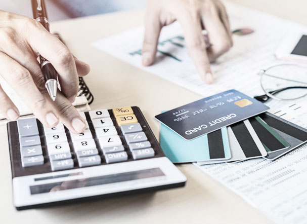 A person doing math on a calculator. Next to it, on the table, several credit cards and sheets of paper
