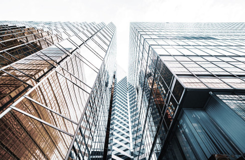 Visão inferior de dois prédios com janelas espelhadas, posicionados lateralmente um com o outro