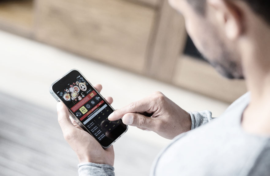 a man in a gray shirt with his back to the image, fiddling with his cell phone on a sports betting website