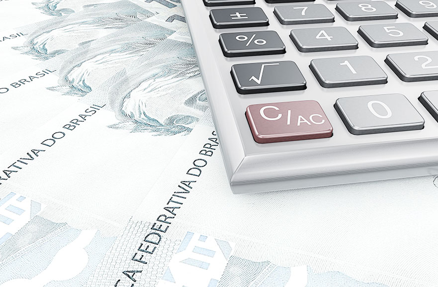 Calculadora cinza, com botões em cinza, preto e vermelho, posicionada acima de cédulas de reais