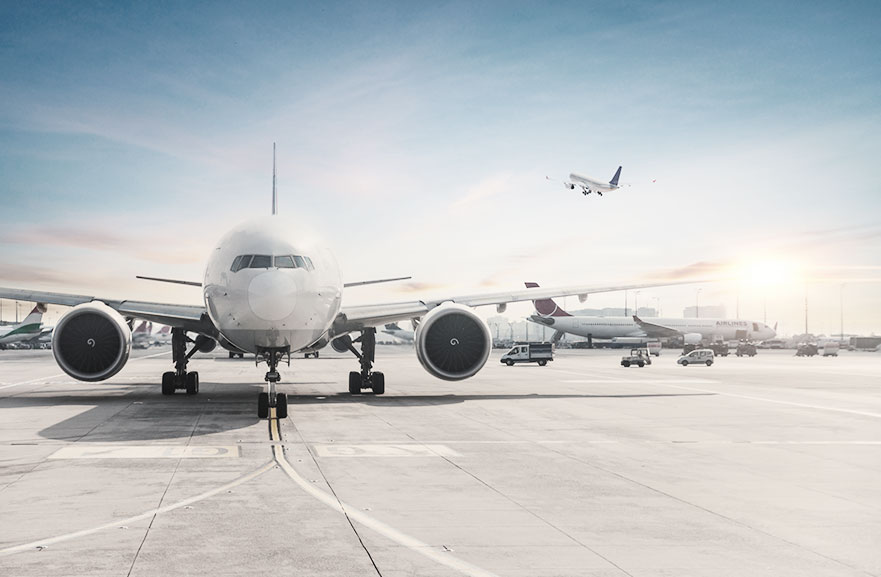 Visão frontal de aeronave branca pousada em pista de decolagem. Mais ao fundo, outras aeronaves pousadas e uma fazendo decolagem