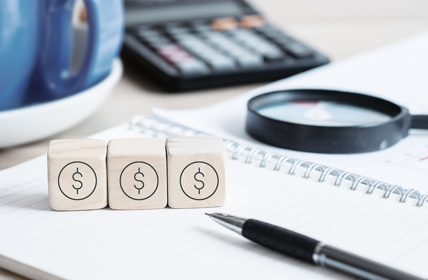 Blocos de madeira 3d posiconados acima de caderno com folhas brancas. Mais ao fundo, calculadora preta com teclas brancas e vermelhas e lupa na cor preta.