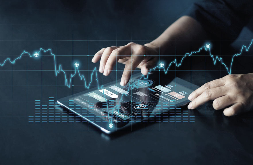 A white person is typing on a tablet positioned on a gray table. On the tablet's screen is information about the financial market