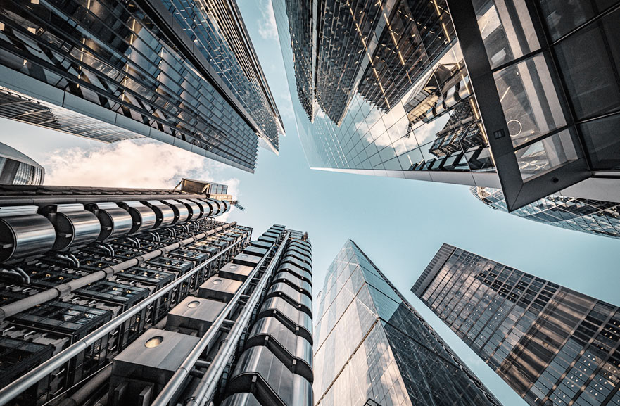 Visão inferior de conjunto de prédios espelhados, num centro urbano.
