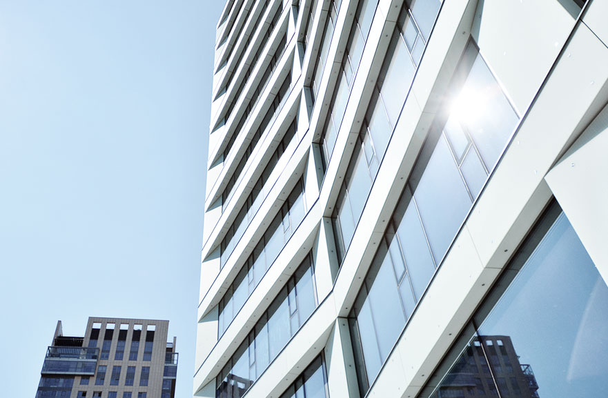 Visão inferior de prédio com paredes brancas e janelas de vidro espelhadas