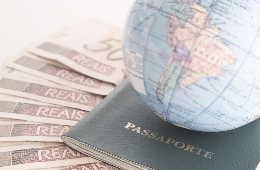 Globo terrestre decorativo acima de passorte na cor preta. Abaixo, várias cédulas de 50 reais lado a lado