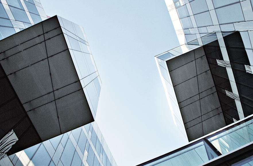 Lower view of two mirrored buildings, one facing the other.