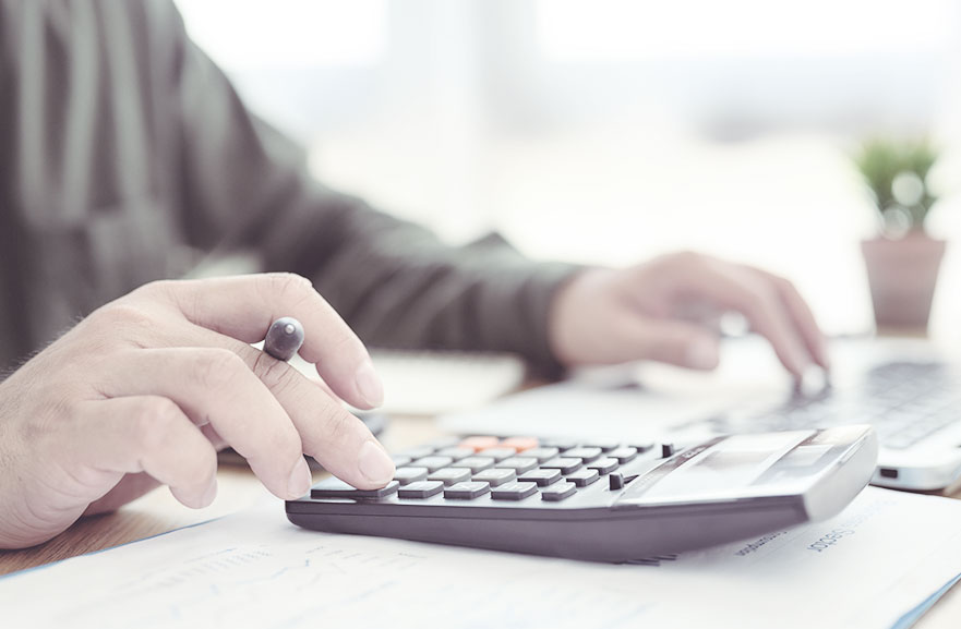 Pessoa usando calculadora e segurando caneta para anotar os resultados em folha A4