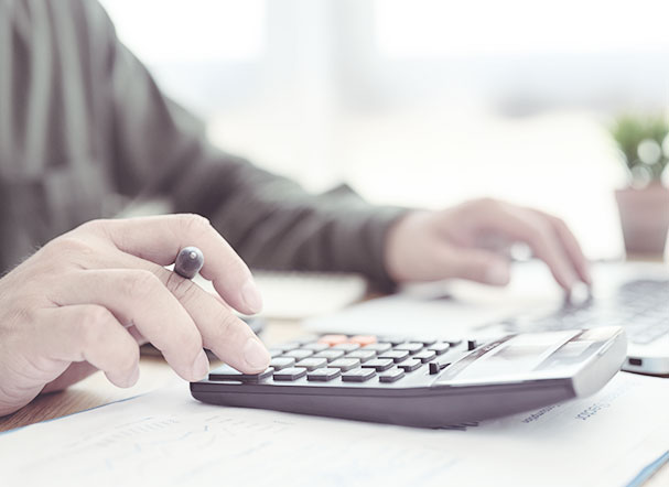 Pessoa usando calculadora e segurando caneta para anotar os resultados em folha A4