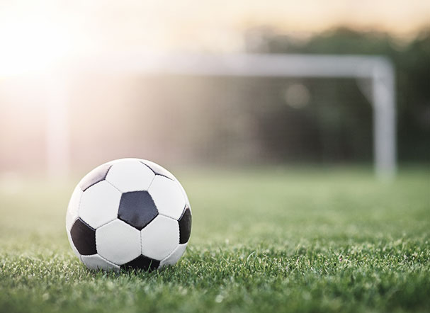 A soccer ball with the colors black and white on a soccer field. In the background, a goal with white goalposts