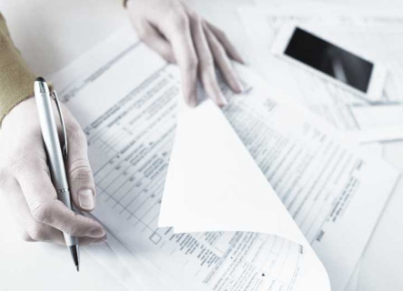 Top view of person holding pen in right hand and checking documents with right hand